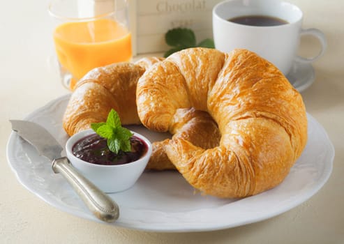 Delicious continentl breakfast with crisp golden croissants, jam and orange juice served on a plate