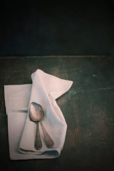 Folded plain white linen napkin and teaspoons on an old dark wooden table with copyspace