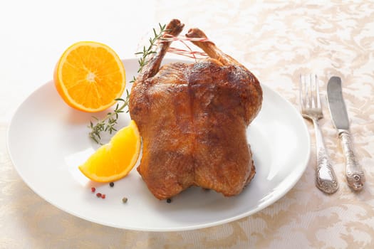 Golden crisp roast chicken or duck served whole on a plate accompanied by sliced orange and rosemary