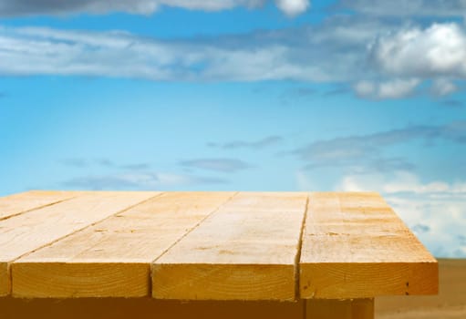Empty wooden table top against a blue sky with fluffy white clouds for the placement of your food or product