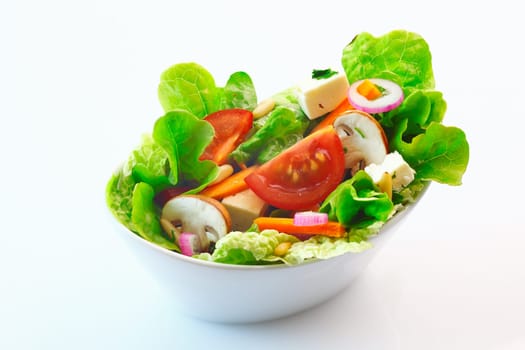 Bowl of fresh mixed green salad with lettuce, tomato, cheese, onion and sliced mushrooms over a white background