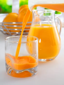 Pouring a glass of fresh healthy orang juice from a jug with a full glass pitcher of juice standing ready in the background