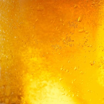 A background created from a closeup of cold light beer in a glass, with condensation droplets on the outside of the glass