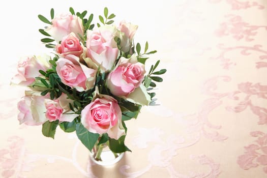 High angle view of a bouquet of fresh pink roses with greenery arranged in a glass vase with copyspace
