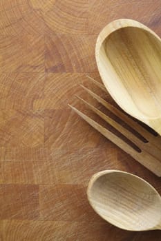 Wooden salad servers with woodgrain lying on a wood chopping board with texture, scratches and copyspace