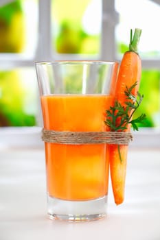 Delicious healthy liquidised carrot juice in a tall glass with a fresh whole carrot tied to the side with string
