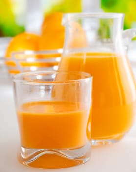 Glass and jug of vibrant colourful healthy fresh orange juice standing on a kitchen table ready for breakfast