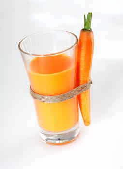 Tall glass of fresh vegetarian carrot juice with an attached whole carrot standing on a white studio background