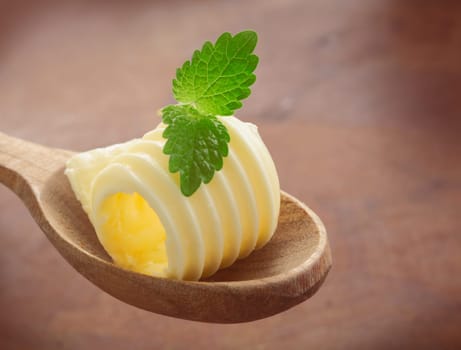 Gourmet rolled creamy butter curl garnished with a fresh sprig of mint served on a wooden salad spoon over a wood background with copyspace