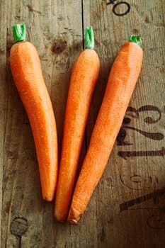A trio of trimmed fresh carrots on rustic wooden packing crate background