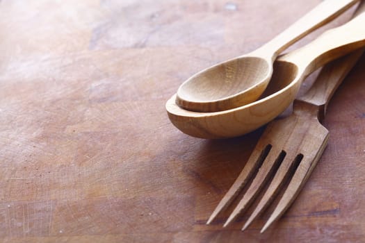 Handcrafted wooden kitchen utensils with a fork and spoons in two sizes lying on a wood surface with copyspace