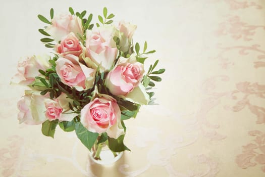High angle view of a bunch of delicate fragrant fresh pink roses arranged in a glass vase with greenery and copyspace