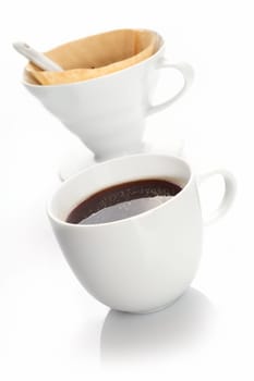 Cup of rich black coffee prepared with a portable white china filter and filter paper used to produce individual portions