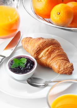 Healthy Continental breakfast with a crisp golden croissant served with jam on a plate alongside freshly squeezed orange juice and whole fruit