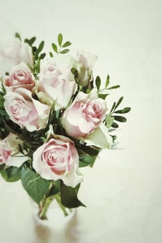 High angle view of a fresh bouquet of delicate pink roses arranged with foliage in a glass vase over a white background with copyspace