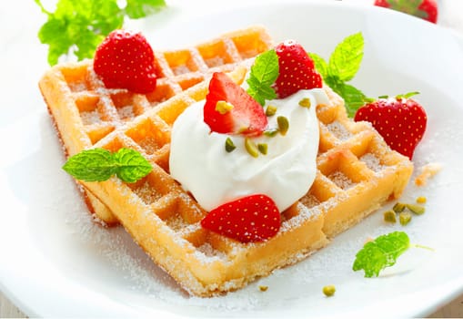 Golden waffle topped with fresh sliced strawberries and cream and sprinkled with sugar for a delicious dessert