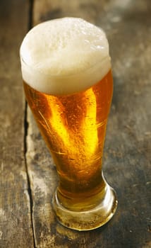 High angle view of a tall glass of chilled beer with a frothy head standing on an old grunge wooden table