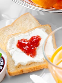 Strawberry jam in the shape of a heart on thick whipped cream topping a slice of fresh white bread