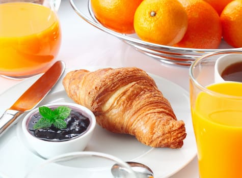 Table setting with a tasty Continental breakfast including fresh oranges and orange juice, strawberry jam and a crisp flaky croissant