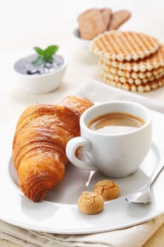 Golden crisp flaky croissant and a cup of rich espresso served with two little macaroons on a plate in a restaurant
