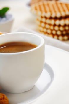 Cropped closeup view of a plain white ceramic cup filled with rich strong espresso coffee served with waffles for breakfast