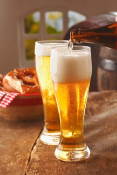 Pouring glasses of frothy golden beer into tall glasses from a brown glass bottle in a pub or restaurant