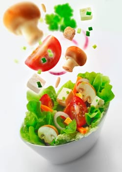 Individual side bowl of healthy fresh mixed green salad of lettuce, carrot, onion, mushrooms, tomato and feta with additional ingredients in th air receding into the distance on a white background