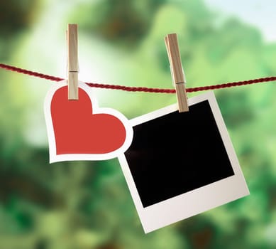 Romantic Valentine memories and greeting card with a pretty white-bordered red heart hanging on an outdoor line with a blank instant photo frame for your image or message