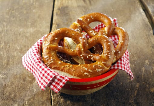 Crisp golden-brown pretzels coated in seeds in a bowl with a colourful checked red and white napkin on a rustic wooden table