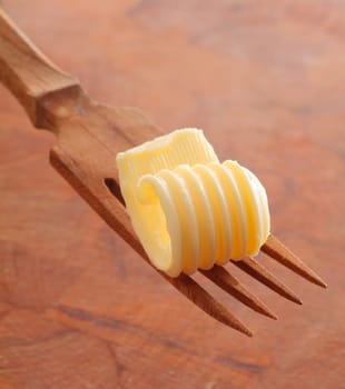 Rolled ridged creamy butter curl balanced on a wooden salad fork over a wood background