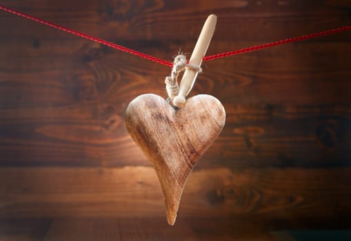 Rustic Valentines greeting card with an elegantly shaped handcrafted wooden textured heart hanging from a peg on a string against a woodgrain timber background with vignetting