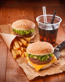 Two hamburgers and fries on brown paper with glass of softdrink
