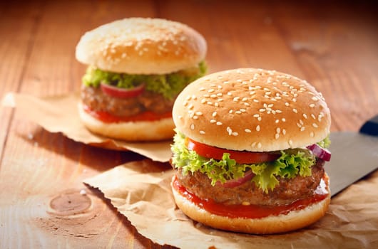 Two hamburgers and french fries with sesame bun on brown paper