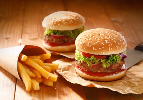 Two hamburgers and french fries with sesame bun on brown paper