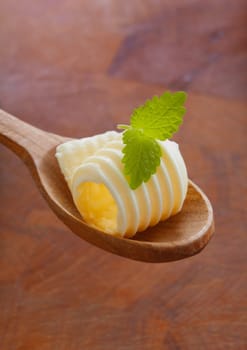Gourmet shaving or curl of rolled butter or margarine garnished with fresh mint being offered on a wooden salad spoon against a wood background