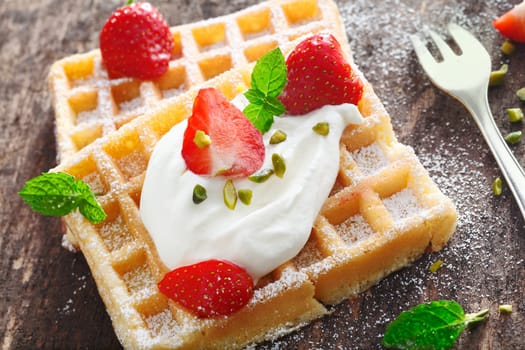 Closeup of a dollop of fresh whipped cream and sliced fresh strawberries topping a crisp golden waffle