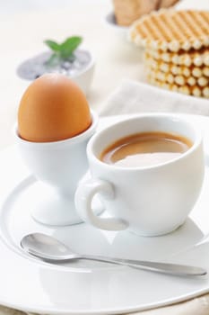 Freshly boiled brown egg in an eggcup served on a plate with a cup of strong espresso coffee for breakfast