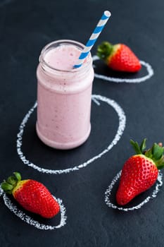 Strawberry smoothie with striped straw and whole strawberries on dark background