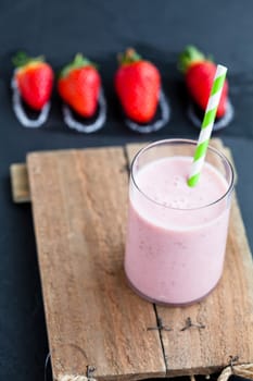 Strawberry smoothie with striped straw and whole strawberries on dark background