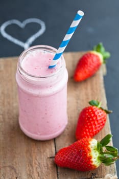 Strawberry smoothie with striped straw and whole strawberries with chalk heart drawing