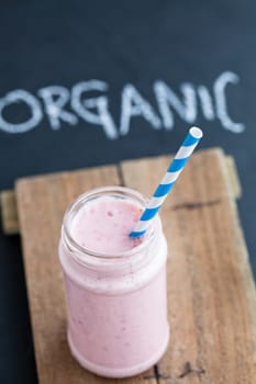 Strawberry smoothie with striped straw on wooden serving tray