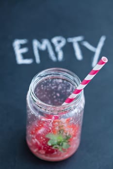 Empty strawberry smoothie glass with striped straw and chalk text on dark background