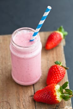Strawberry smoothie with striped straw and whole strawberries on wooden serving tray