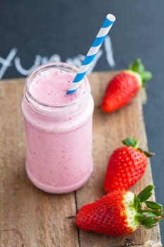Strawberry smoothie with striped straw and whole strawberries on wooden serving tray
