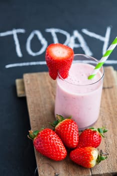 Strawberry smoothie with striped straw and whole strawberries on wooden serving tray