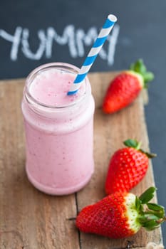 Strawberry smoothie with striped straw and whole strawberries on wooden serving tray