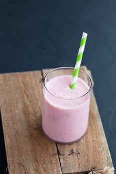 Strawberry smoothie with striped straw on wooden serving tray on dark background