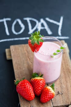 Strawberry smoothie with striped straw and whole strawberries on wooden serving tray