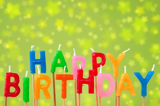 Colorful candles forming the sentence "happy birthday"" on the green blurry background"