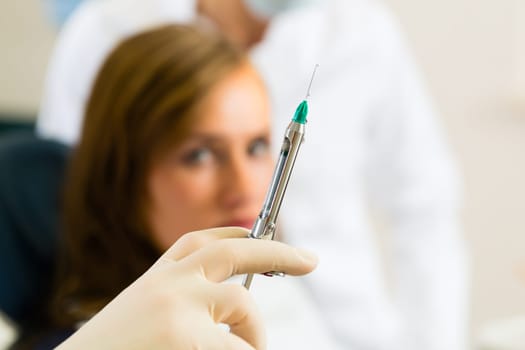 Dentist holding a syringe,female patient and dental assistant in the background